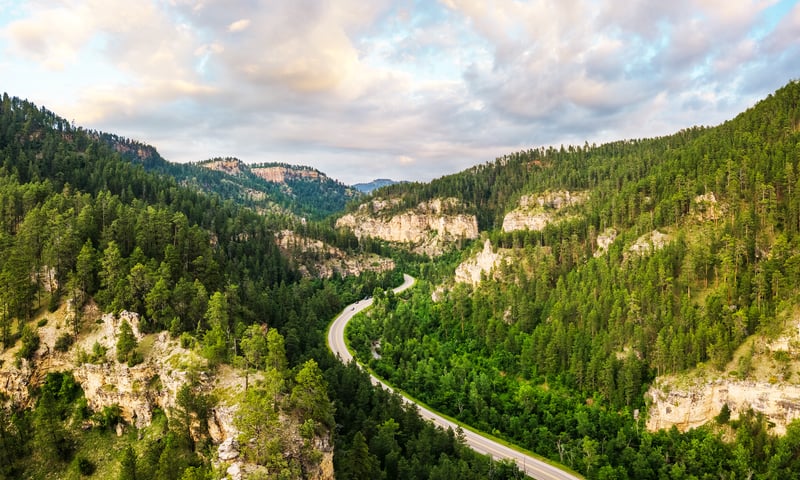 Travel East through Spearfish Canyon Scenic Byway, winding beneath towering limestone cliffs.